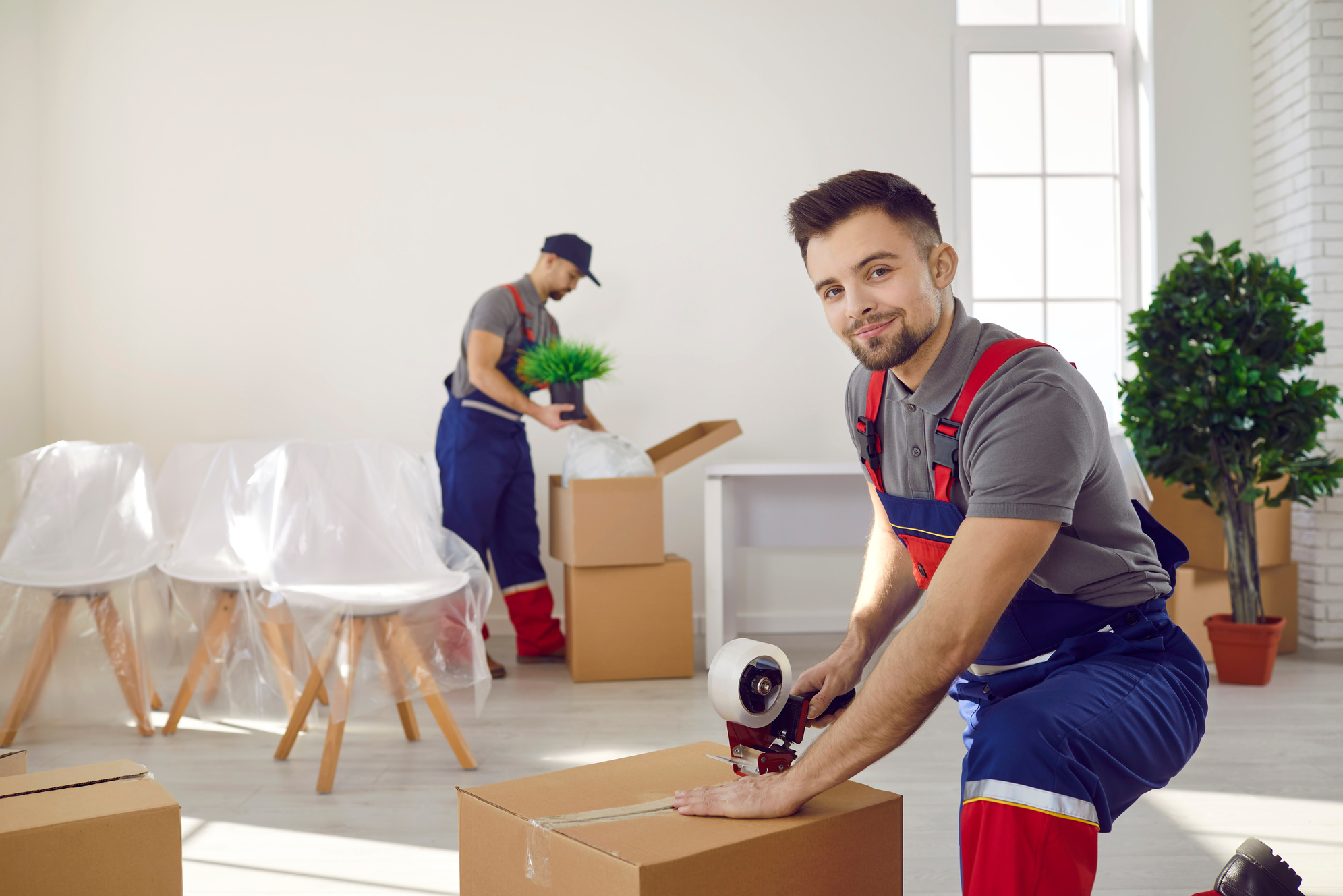 Young Man from Moving Company or Delivery Service Sealing Box Using Tape Dispenser